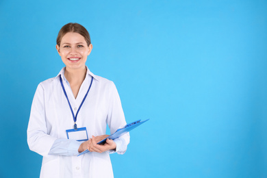 Photo of Portrait of young doctor with clipboard on blue background, space for text