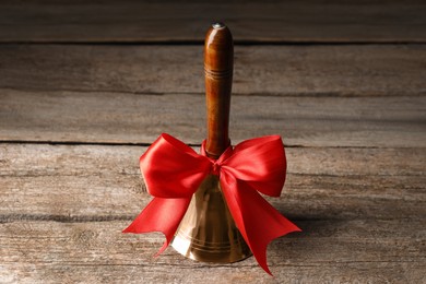 Golden bell with red bow on wooden table. School days