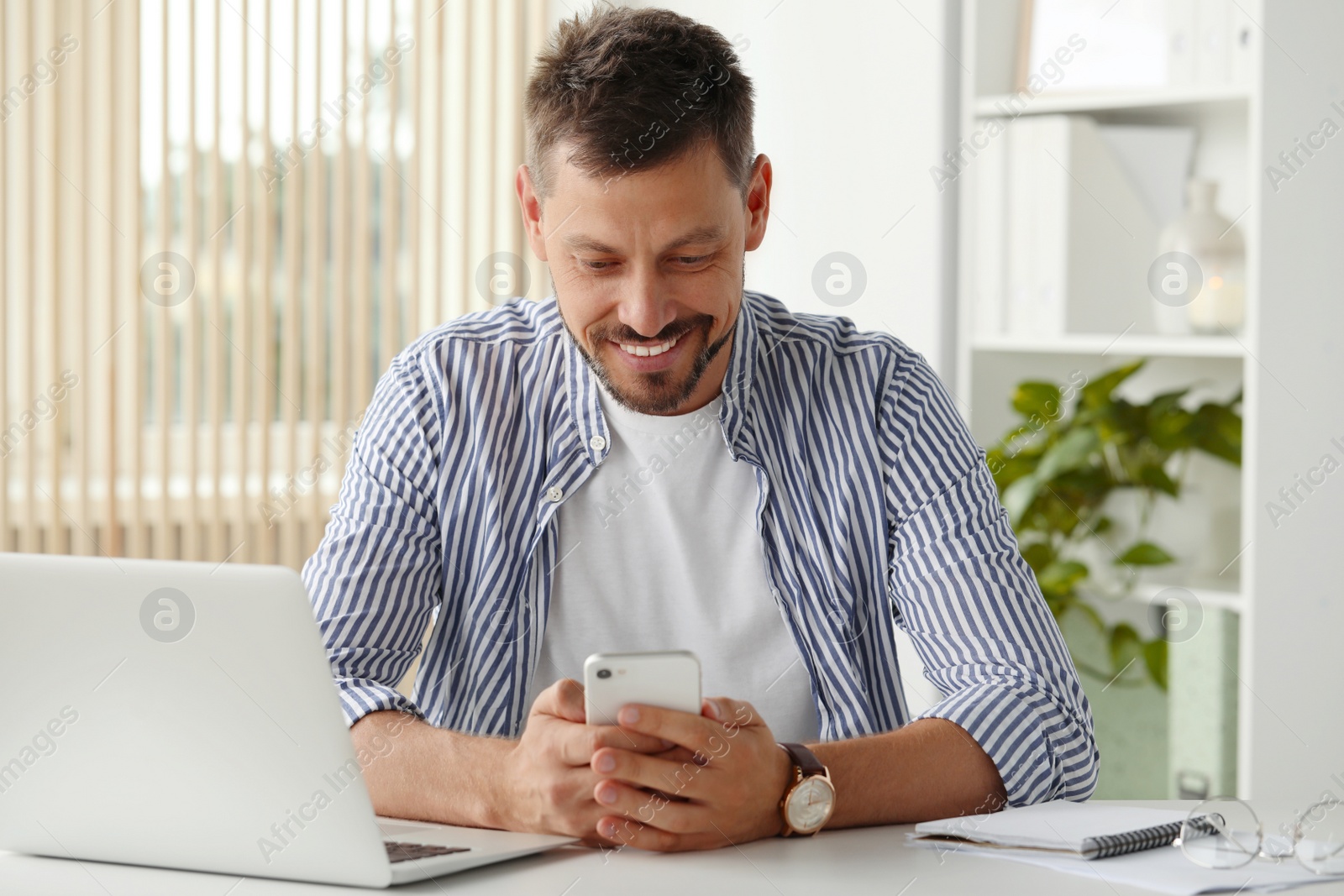 Photo of Happy man using smartphone while working with laptop in office