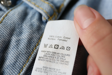 Photo of Woman reading clothing label with care symbols and material content on jeans, closeup