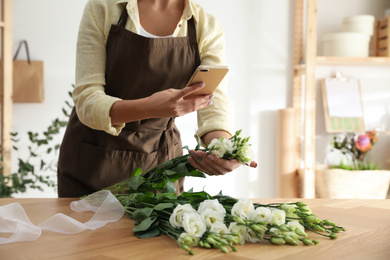 Photo of Florist taking picture of beautiful flowers in workshop, closeup