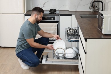 Photo of Smiling man loading dishwasher with plates in kitchen