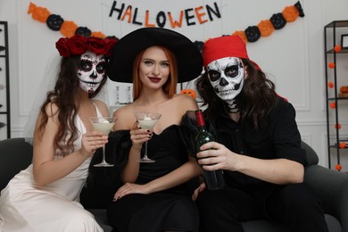 Group of people in scary costumes with cocktails celebrating Halloween indoors