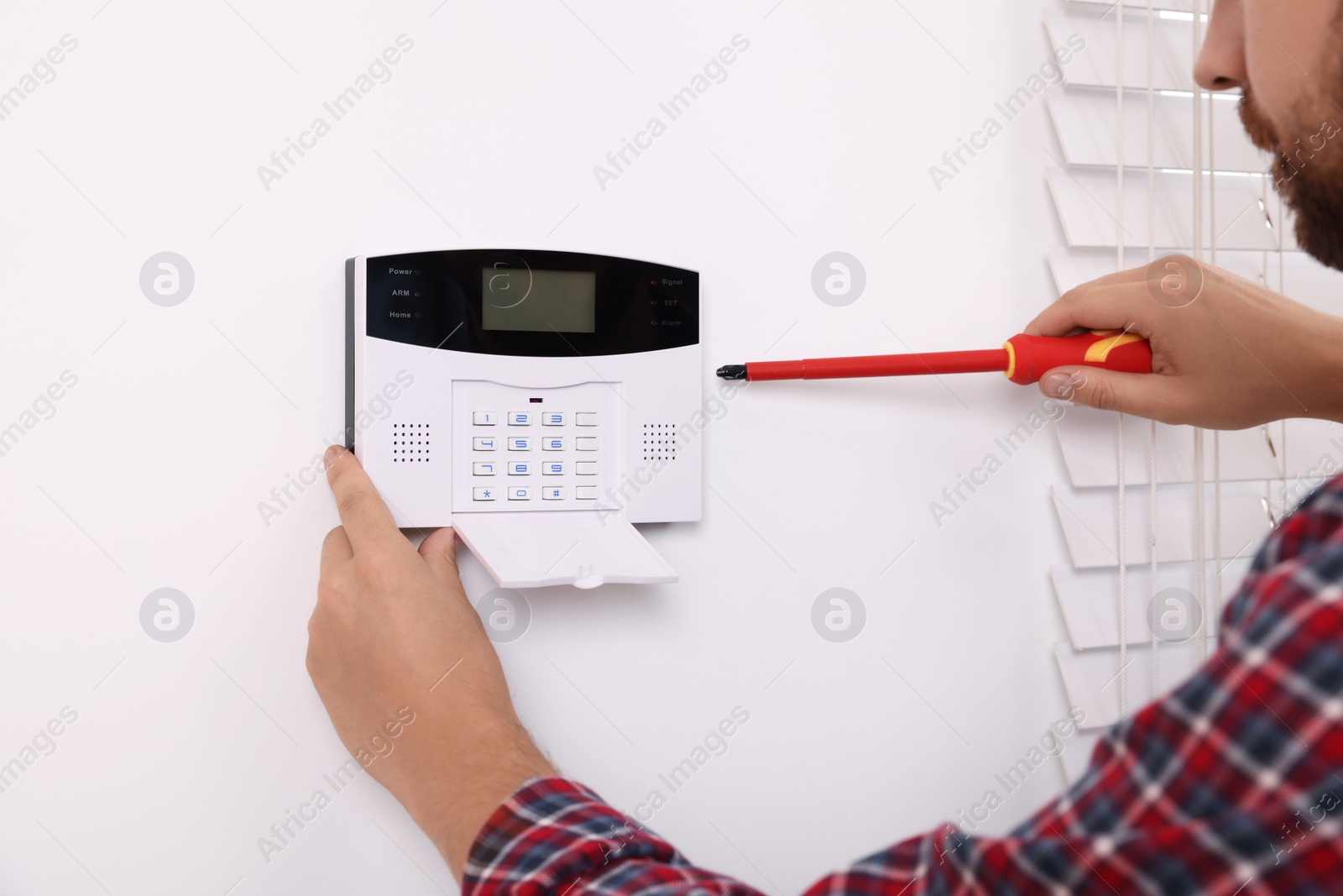 Photo of Man installing home security alarm system on white wall indoors, closeup