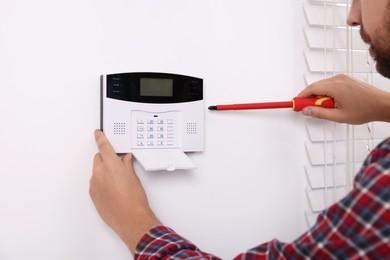 Man installing home security alarm system on white wall indoors, closeup