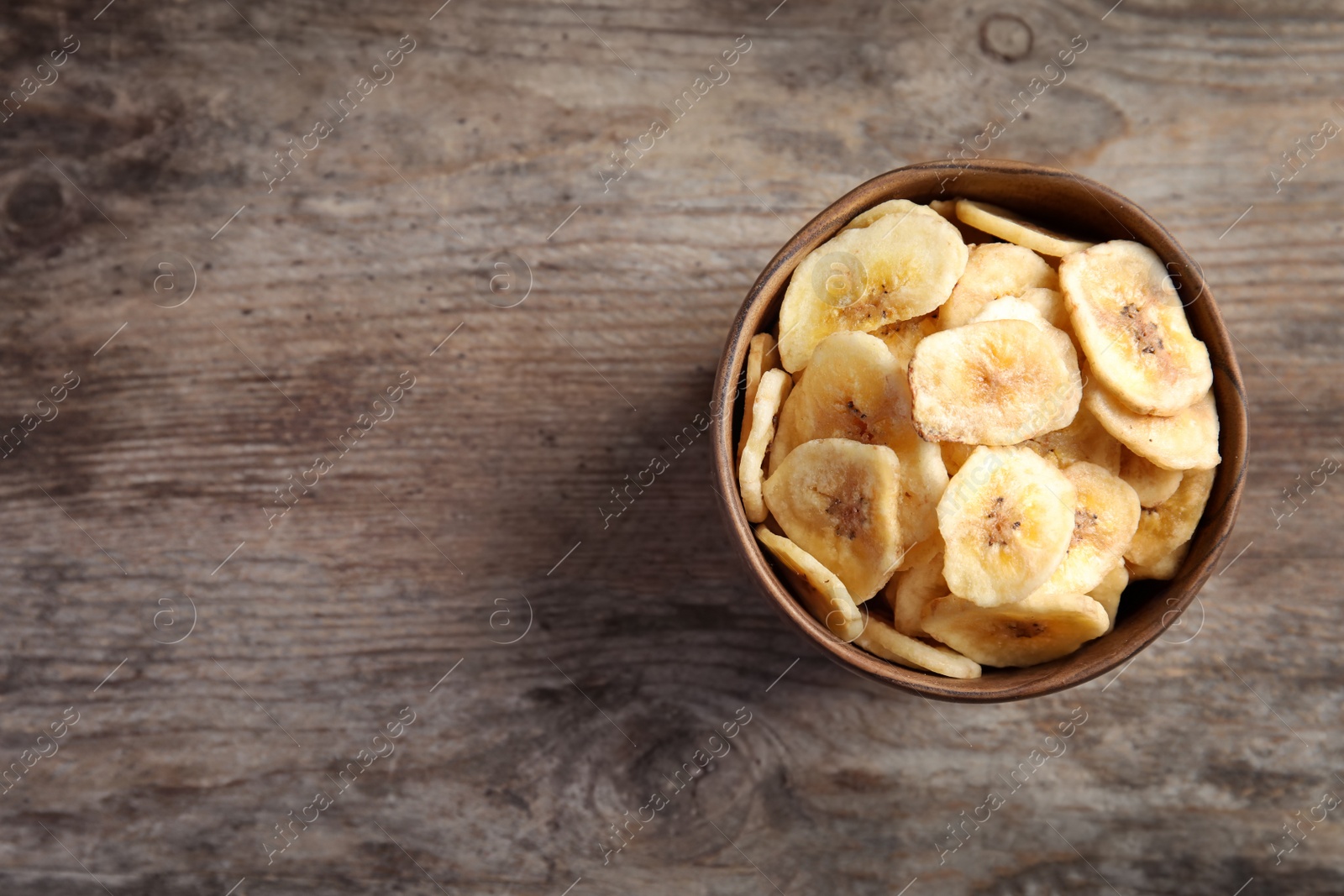 Photo of Bowl with sweet banana slices on wooden  table, space for text. Dried fruit as healthy snack