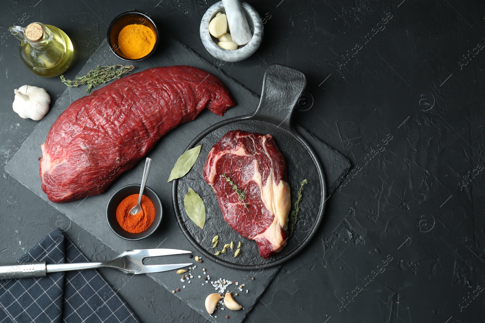 Photo of Pieces of raw beef meat and spices on black table, flat lay. Space for text