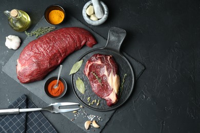 Pieces of raw beef meat and spices on black table, flat lay. Space for text