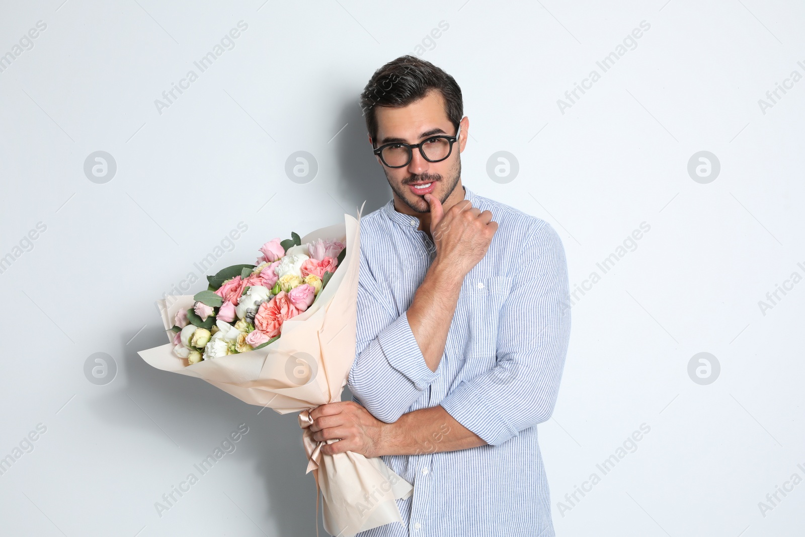 Photo of Young handsome man with beautiful flower bouquet on light background