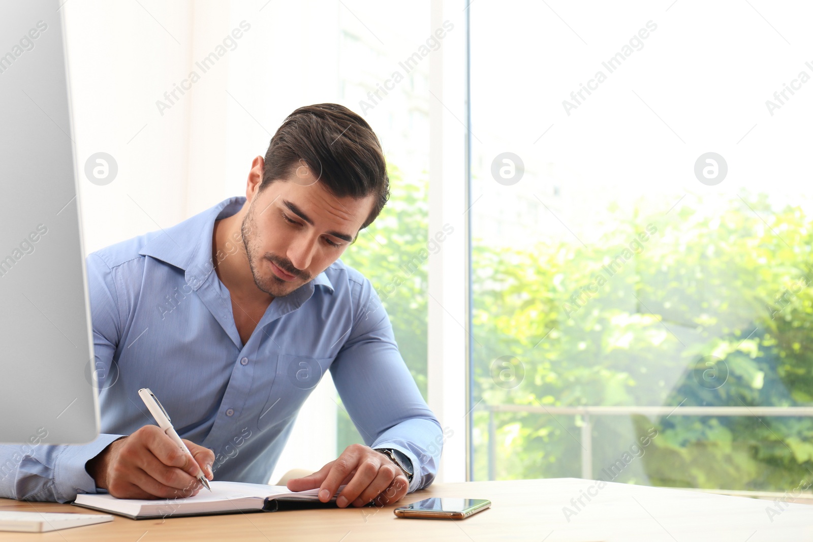 Photo of Handsome young man working with notebook at table in office