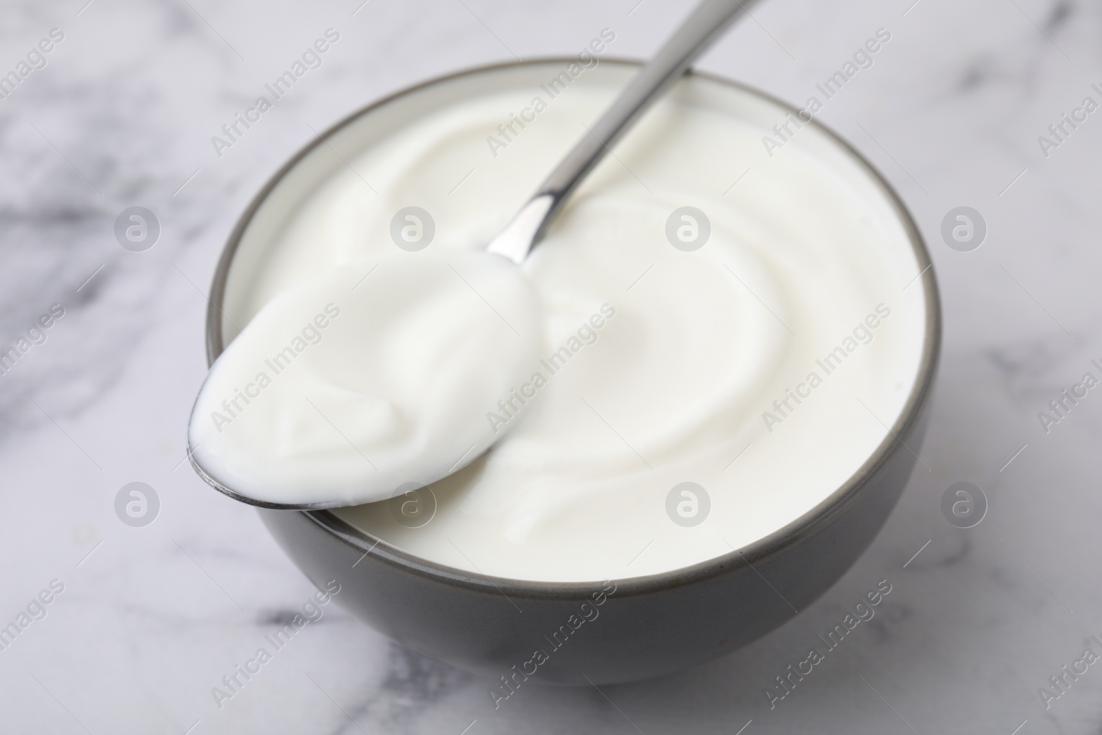 Photo of Delicious natural yogurt in bowl and spoon on white marble table, closeup