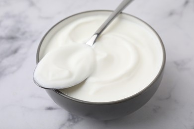 Photo of Delicious natural yogurt in bowl and spoon on white marble table, closeup