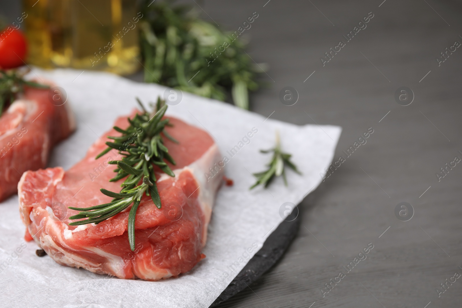 Photo of Fresh raw meat with rosemary on grey wooden table, closeup. Space for text
