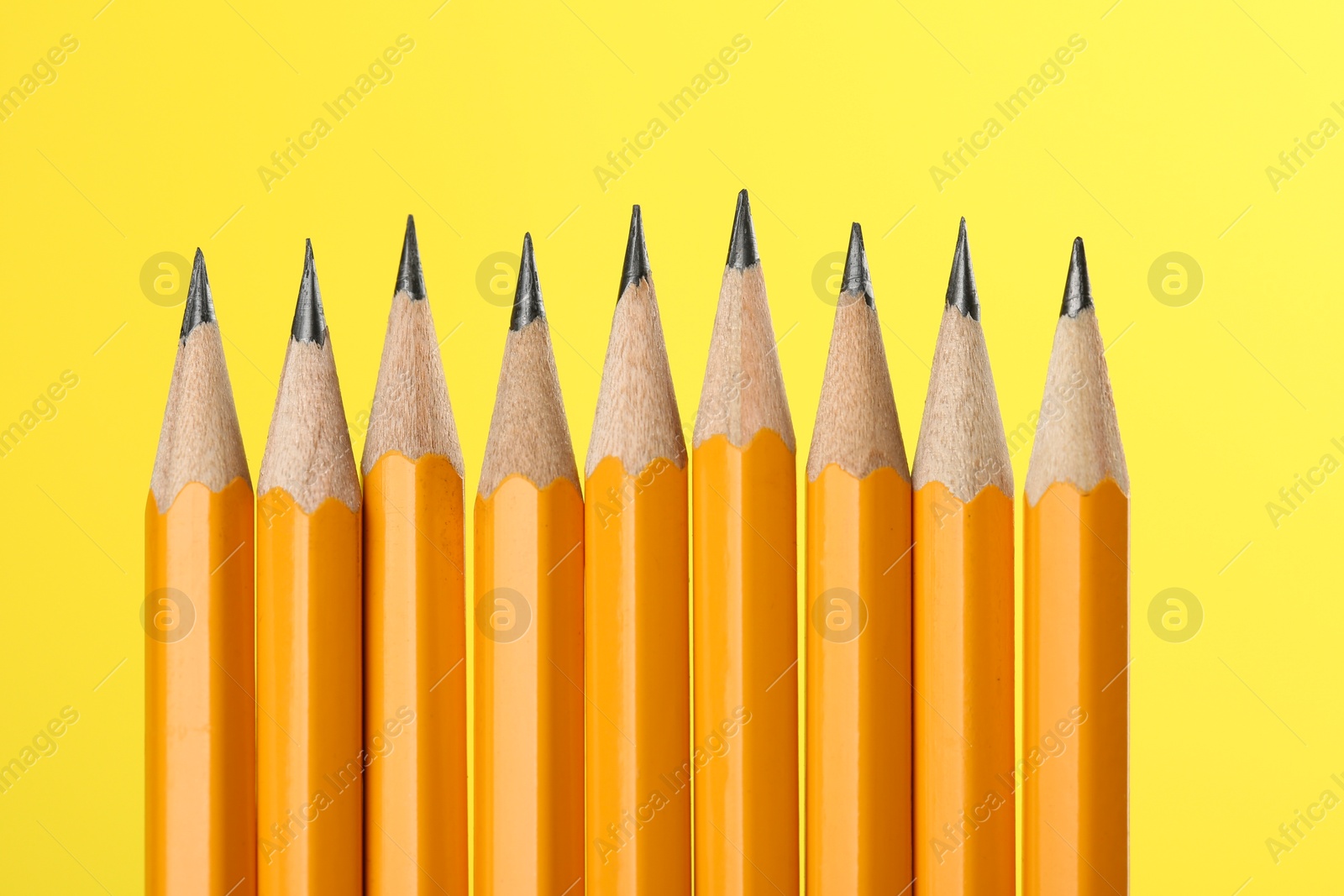 Photo of Many sharp graphite pencils on yellow background, macro view