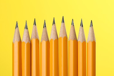 Photo of Many sharp graphite pencils on yellow background, macro view