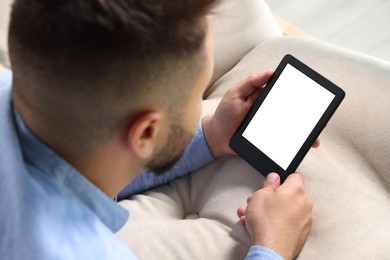 Photo of Man using e-book reader on sofa indoors, closeup