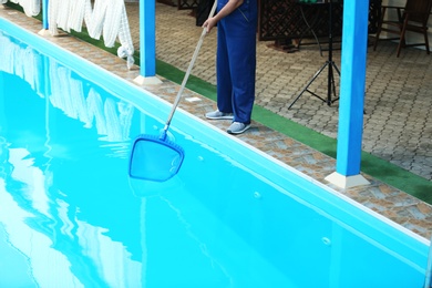 Male worker cleaning outdoor pool with scoop net