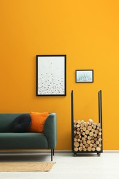 Stylish living room interior with sofa and firewood near orange wall
