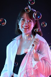 Photo of Portrait of happy woman among bubbles on dark background
