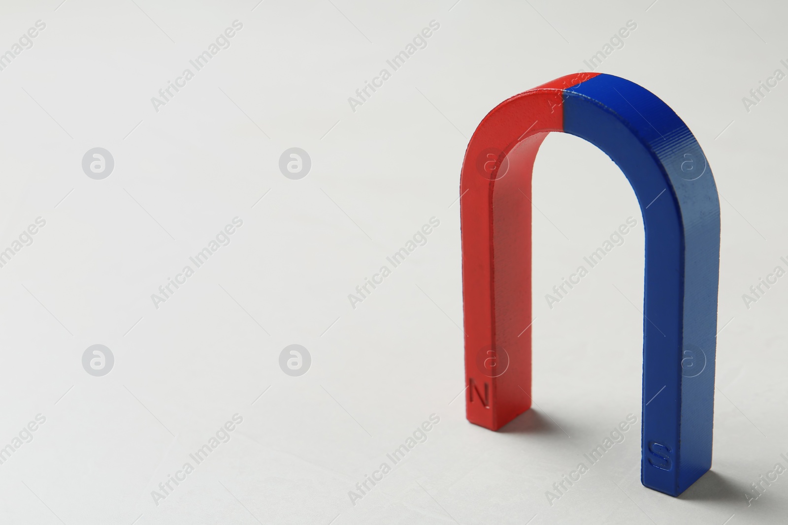 Photo of Red and blue horseshoe magnet on white background. Space for text