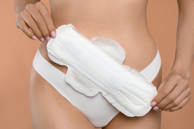 Photo of Woman in white panties with menstrual pad on peach background, closeup