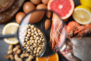 Photo of Different products with magnifier focused on soy beans and shrimps, closeup. Food allergy concept