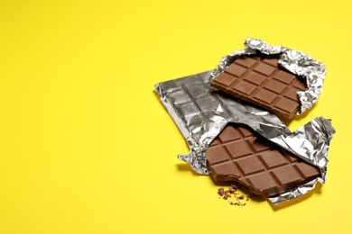 Photo of Delicious chocolate bars on yellow background, space for text