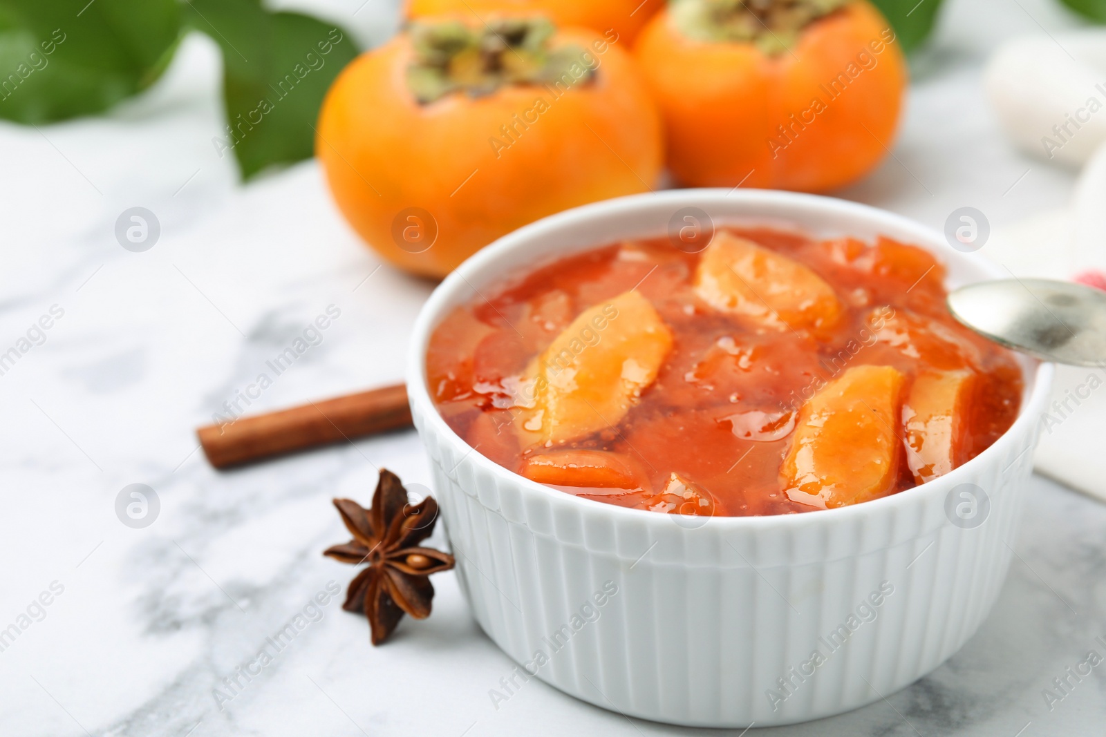 Photo of Bowl of tasty persimmon jam on white marble table, closeup. Space for text