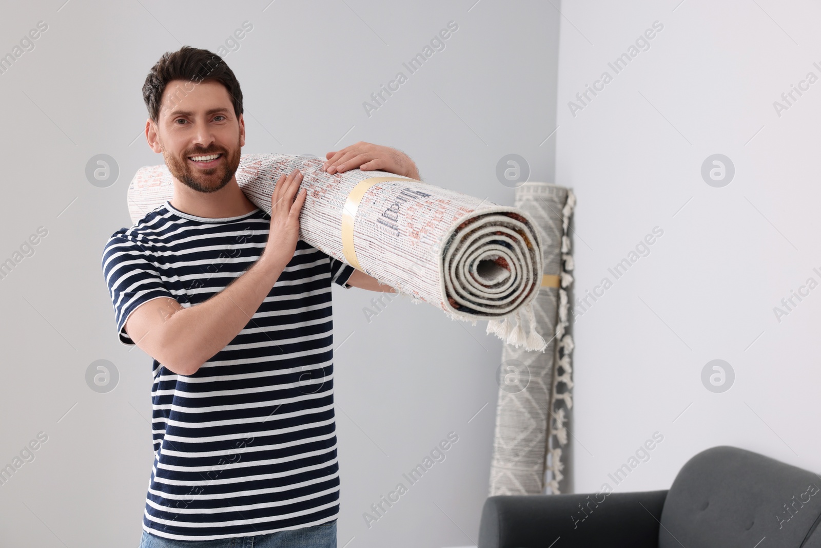 Photo of Smiling man holding rolled carpet in room