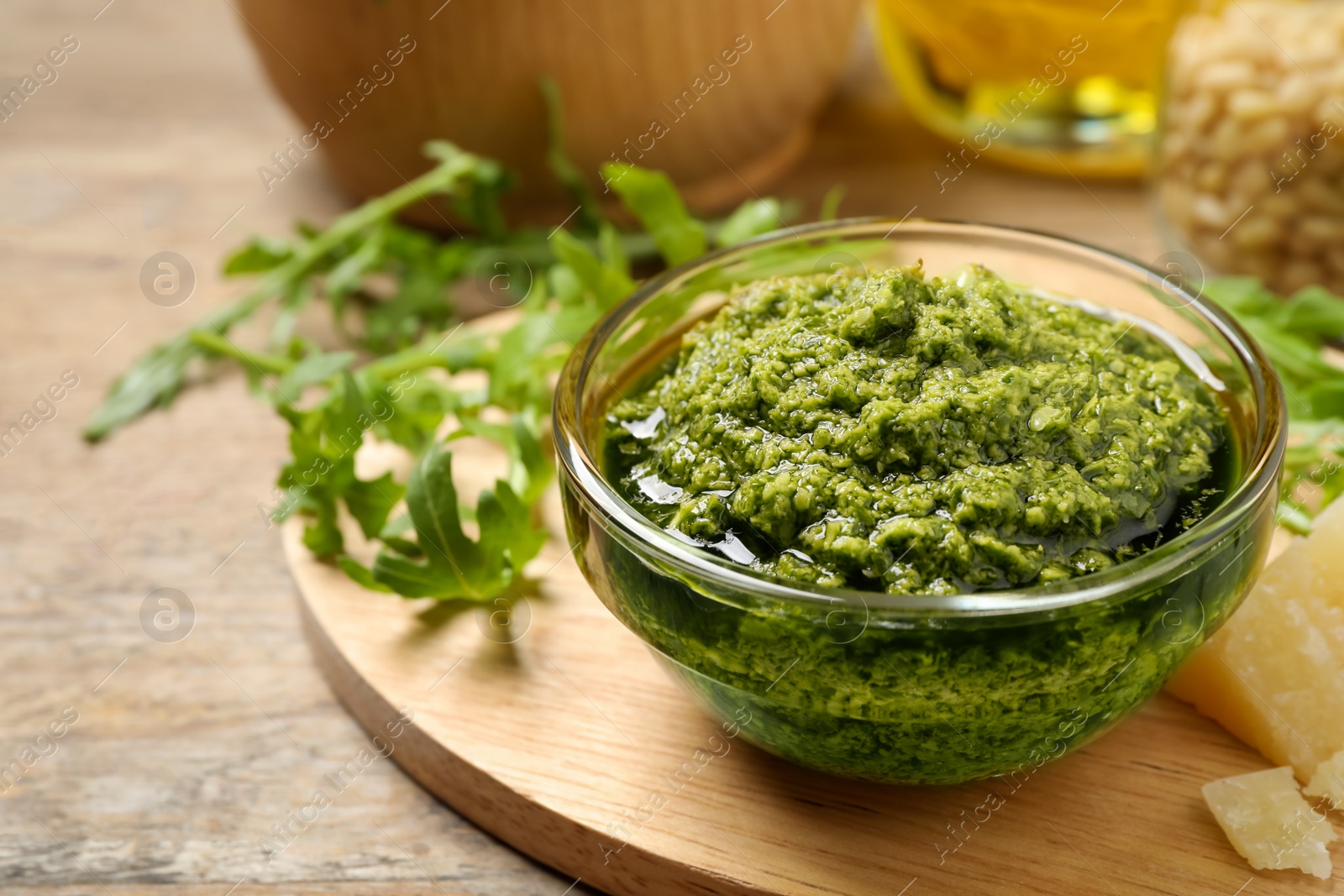 Photo of Bowl of tasty arugula pesto and ingredients on table, closeup