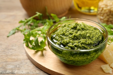 Bowl of tasty arugula pesto and ingredients on table, closeup