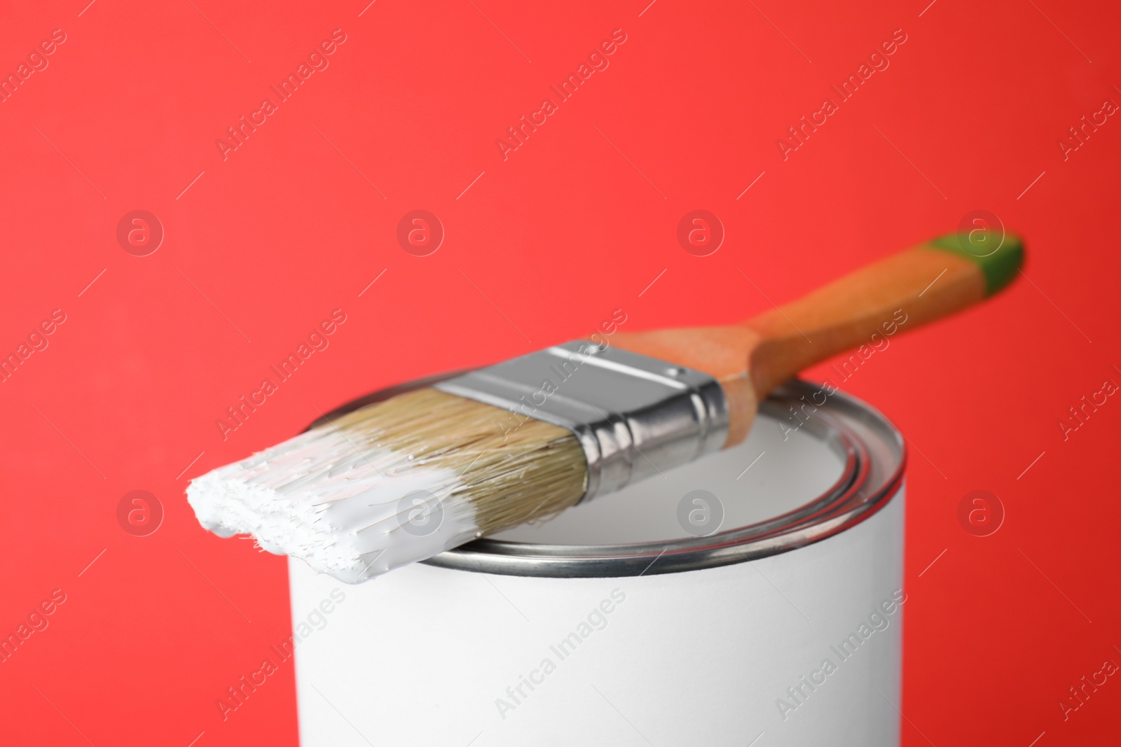 Photo of Can of white paint with brush on red background