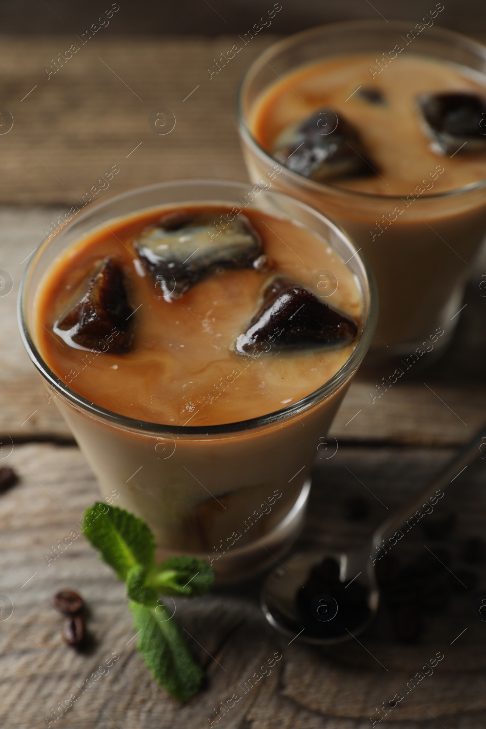 Photo of Glasses of delicious iced coffee with milk, beans and mint on wooden table, closeup