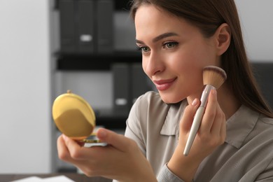 Photo of Young woman with cosmetic pocket mirror doing makeup indoors, closeup