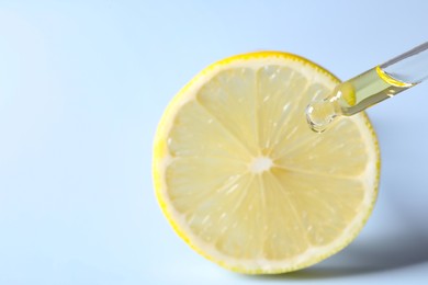 Photo of Dripping cosmetic serum from pipette onto lemon slice against light blue background, closeup. Space for text
