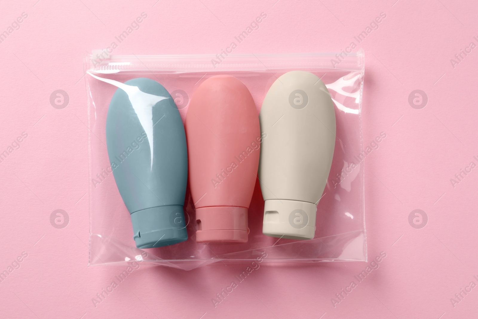 Photo of Cosmetic travel kit in plastic bag on pink background, top view. Bath accessories