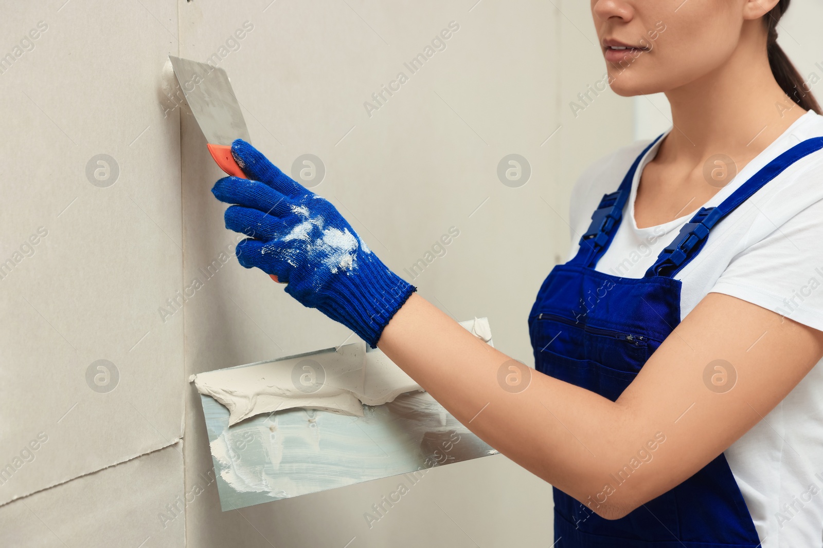 Photo of Professional worker plastering wall with putty knives, closeup