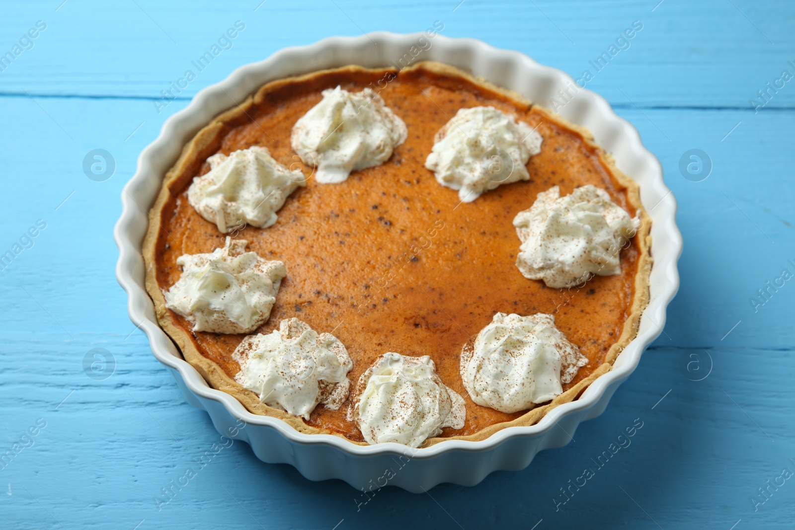 Photo of Delicious pumpkin pie with whipped cream on light blue wooden table