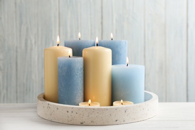 Photo of Burning different candles in tray on table