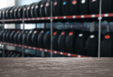 Image of Empty wooden surface and blurred view of car tires in auto store, closeup. Space for text 