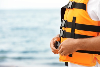 Photo of Male lifeguard putting on life vest near sea, closeup