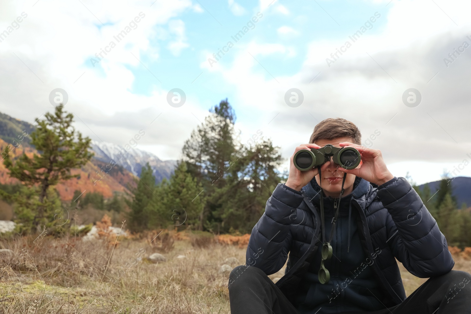 Photo of Boy looking through binoculars in beautiful mountains. Space for text