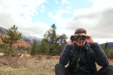 Boy looking through binoculars in beautiful mountains. Space for text