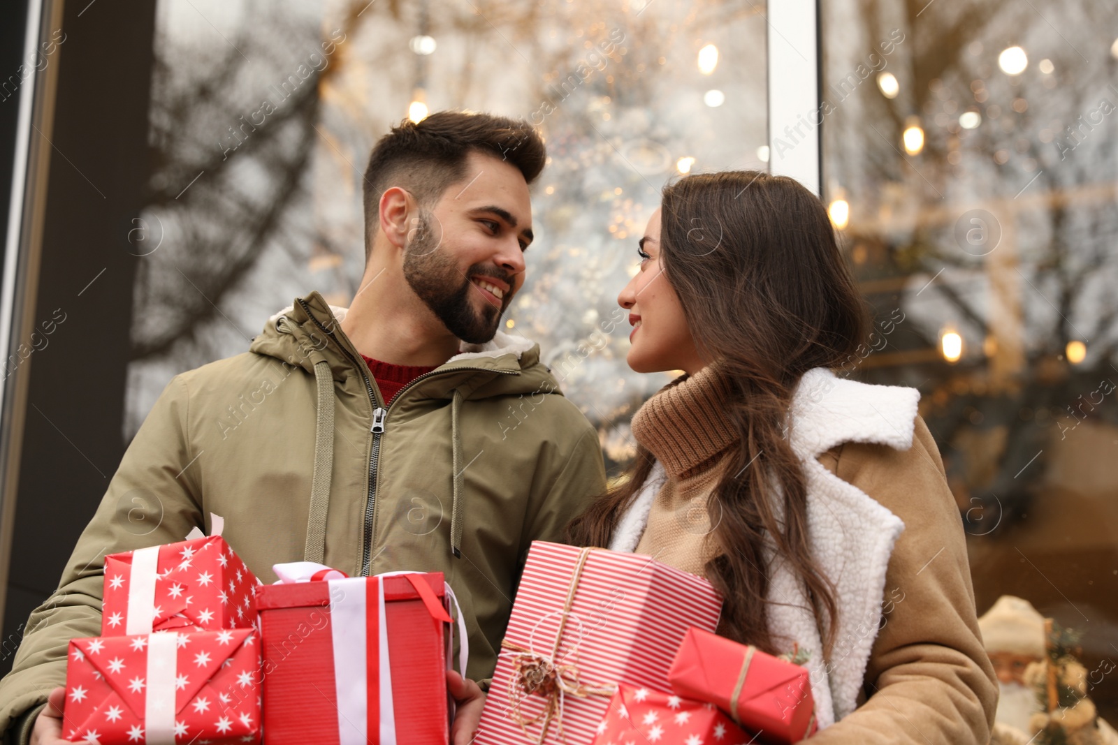 Photo of Lovely couple with Christmas presents near festively decorated store outdoors