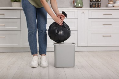 Photo of Woman taking garbage bag out of trash bin in kitchen, closeup