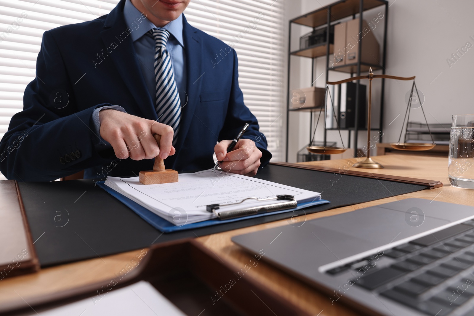 Photo of Notary with pen stamping document at table in office, closeup