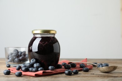 Jar of blueberry jam and fresh berries on wooden table. Space for text