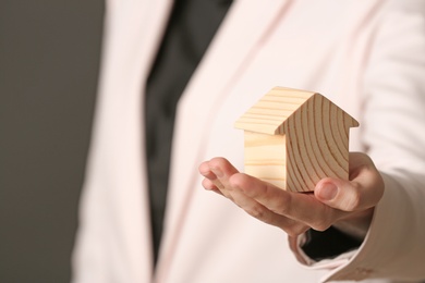 Photo of Female agent holding wooden house model on dark background, closeup. Home insurance