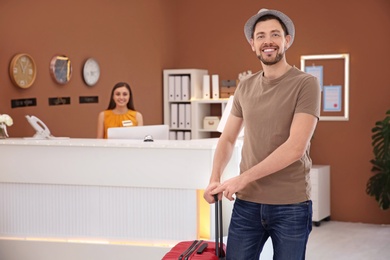 Photo of Young man with luggage near reception desk in hotel