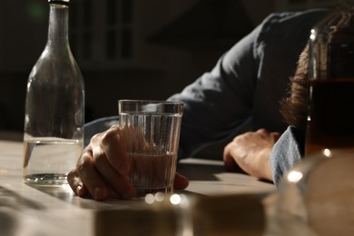Photo of Addicted man with alcoholic drink sleeping at table in kitchen, closeup